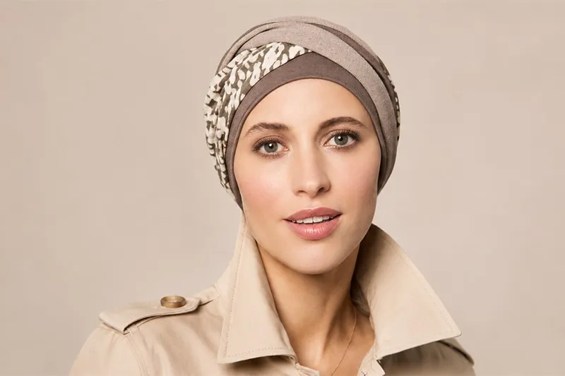 Vrouw draagt een taupekleurige hoofddoek met een gedraaide band in dierenprint, gecombineerd met een beige trenchcoat.